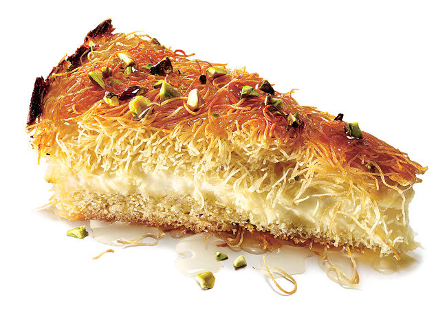 A slice of knafeh with a delicious sauce and topped with chopped pecans